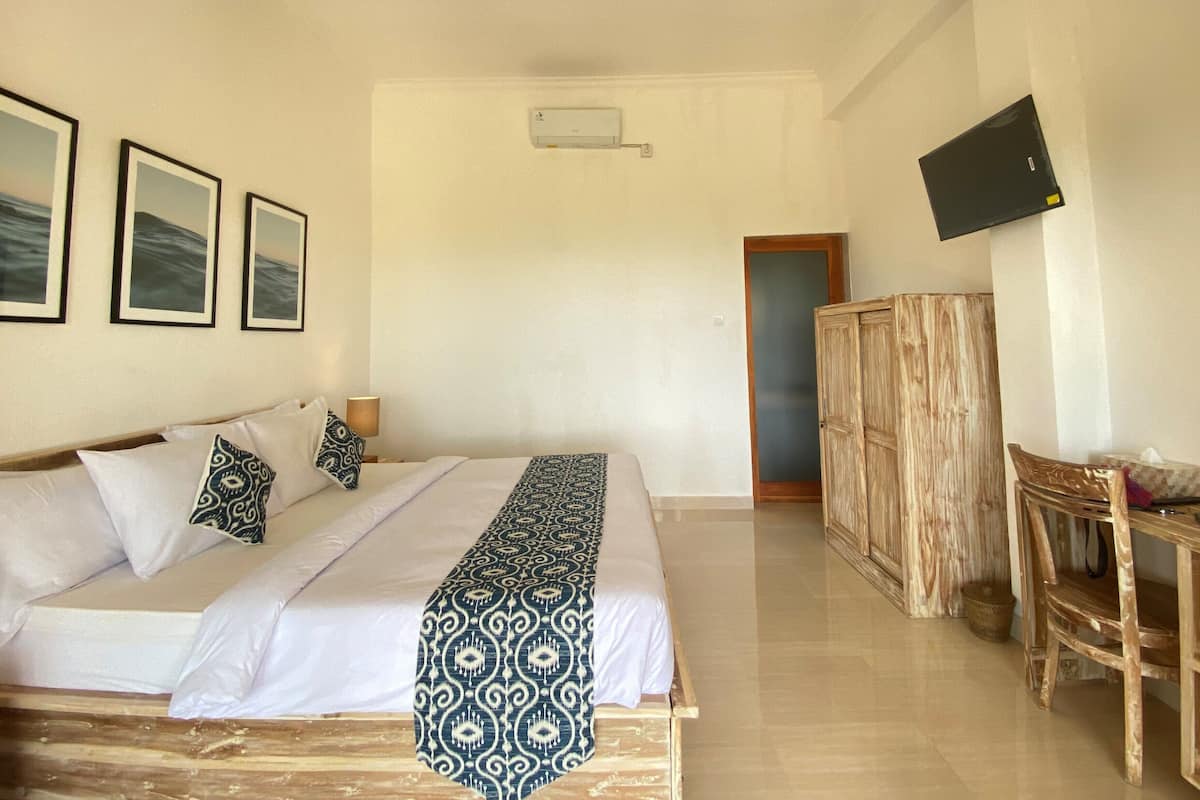 A hotel room with a bed, a TV mounted on the wall, and a wooden wardrobe.
