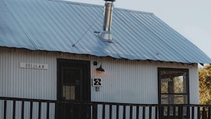 A rustic building with a corrugated metal roof, a chimney, and a wooden porch with a black railing.