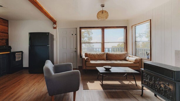 A living room with a sofa, armchair, coffee table, fireplace, and a view of the outdoors through large windows.