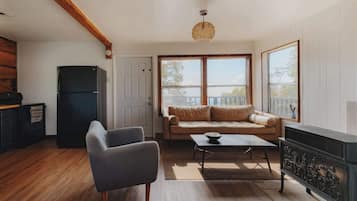 Un salon comprenant un canapé, un fauteuil, une table basse, une cheminée et offrant une vue sur l’extérieur grâce à de grandes fenêtres.