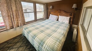 A bedroom with a bed, curtains, a window, and a lamp. - Idlewild at Duck Harbor Resort (Rockaway Beach)