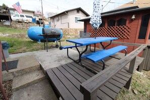 A wooden picnic table with benches, a barbecue grill, and a covered umbrella. - Idlewild at Duck Harbor Resort (Rockaway Beach)