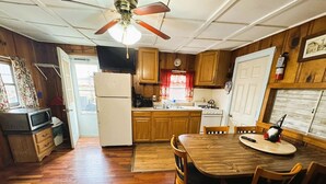 A compact kitchen with wooden cabinets, a refrigerator, a dining table with chairs, and a ceiling fan. - Idlewild at Duck Harbor Resort (Rockaway Beach)