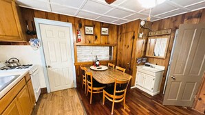 A kitchen with wooden cabinets, a white stove, a dining table with chairs, and a white sink. - Idlewild at Duck Harbor Resort (Rockaway Beach)