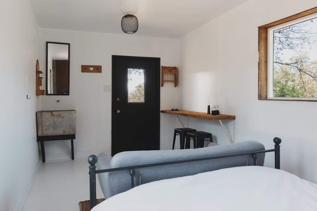 A bedroom with a bed, a desk, a chair, a door, a mirror, and a window.