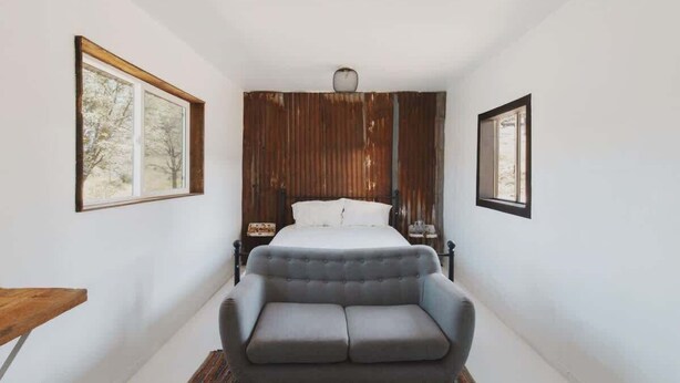 Une chambre à coucher avec un lit, un canapé gris, une tête de lit en bois et deux tableaux encadrés accrochés aux murs.