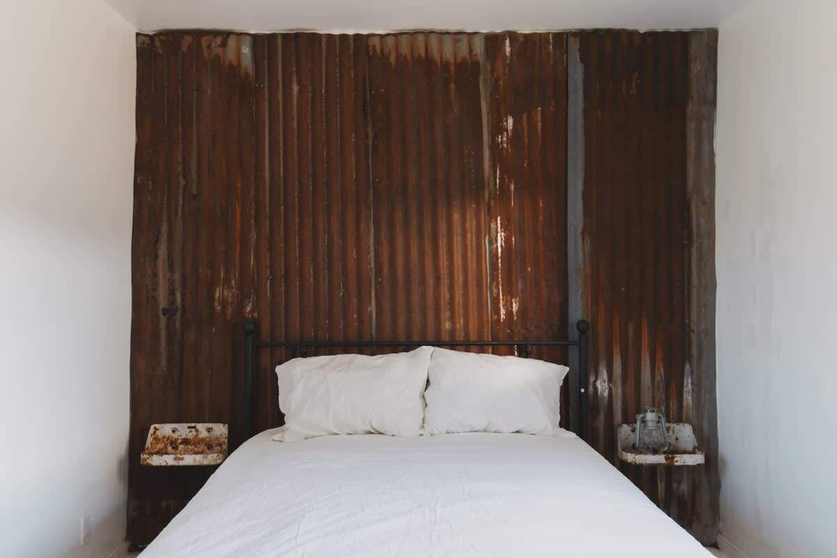 A bed with white bedding in a room with a rustic, corrugated metal wall.