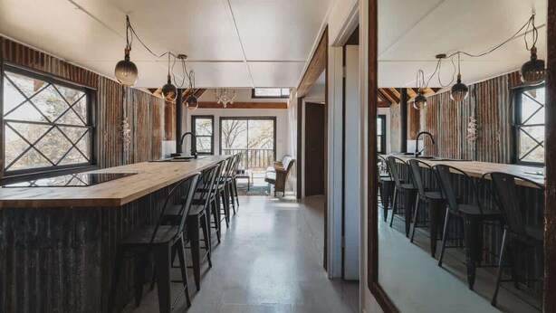 A modern kitchen with a long wooden counter, black chairs, and pendant lighting. - Event venue in nature retreat (Dunlap)