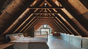 A high-ceilinged attic bedroom with a sloped wooden ceiling, a bed, a small table, and a view through a window. - Event venue in nature retreat (Dunlap)