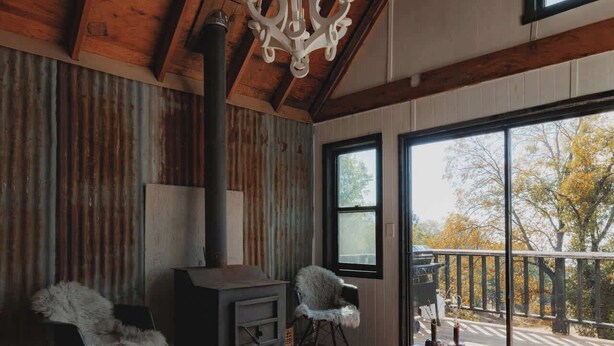 A rustic interior with a wooden ceiling, a fireplace, a large window, and a cozy seating area. - Secluded rustic 3-bedroom cabin on private land (Dunlap)