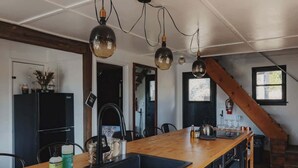 A kitchen with a wooden countertop, black cabinets, and a large island with a sink. There are hanging pendant lights and a view of a staircase. - Secluded rustic 3-bedroom cabin on private land (Dunlap)