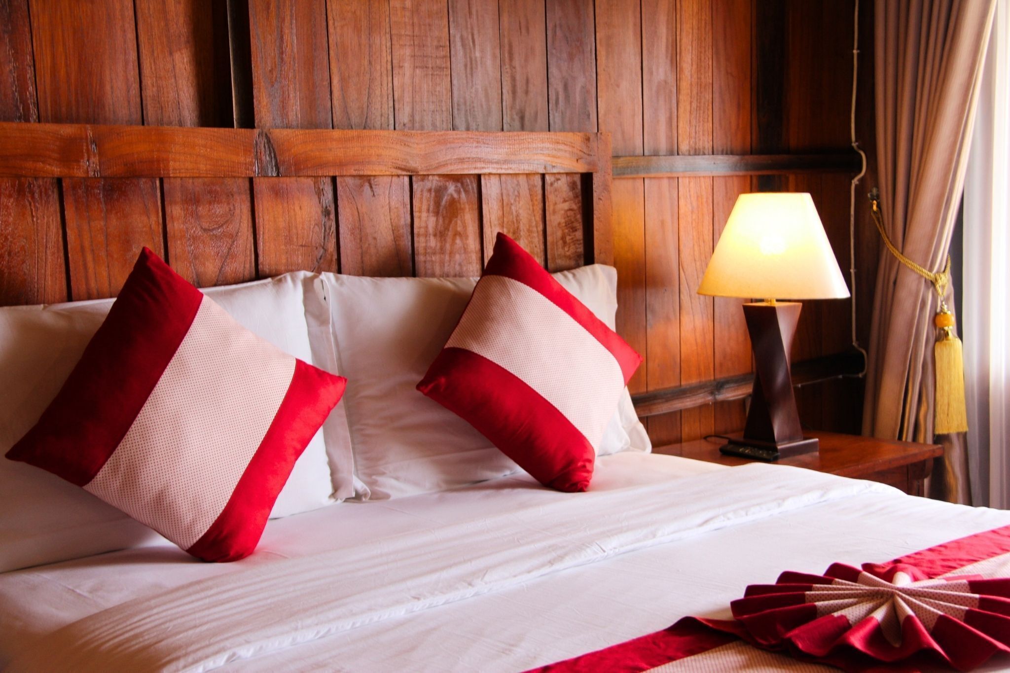 A bed with white and red pillows, a wooden headboard, and a bedside lamp.