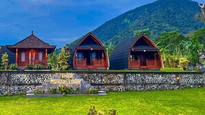 Three traditional wooden houses with a stone wall in front, labeled "PONDOK MUNDUK LUWIS." - Munduk Luwih Ecolodge Bedugul by AGATA (Baturiti)