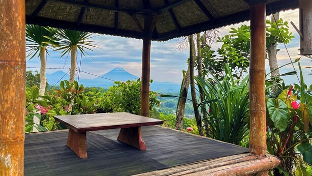 A wooden bench under a thatched roof structure with a view of a mountain. - Munduk Luwih Ecolodge Bedugul by AGATA (Baturiti)