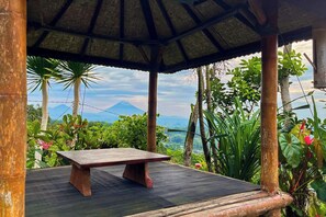 A wooden bench under a thatched roof structure with a view of a mountain. - Munduk Luwih Ecolodge Bedugul by AGATA (Baturiti)