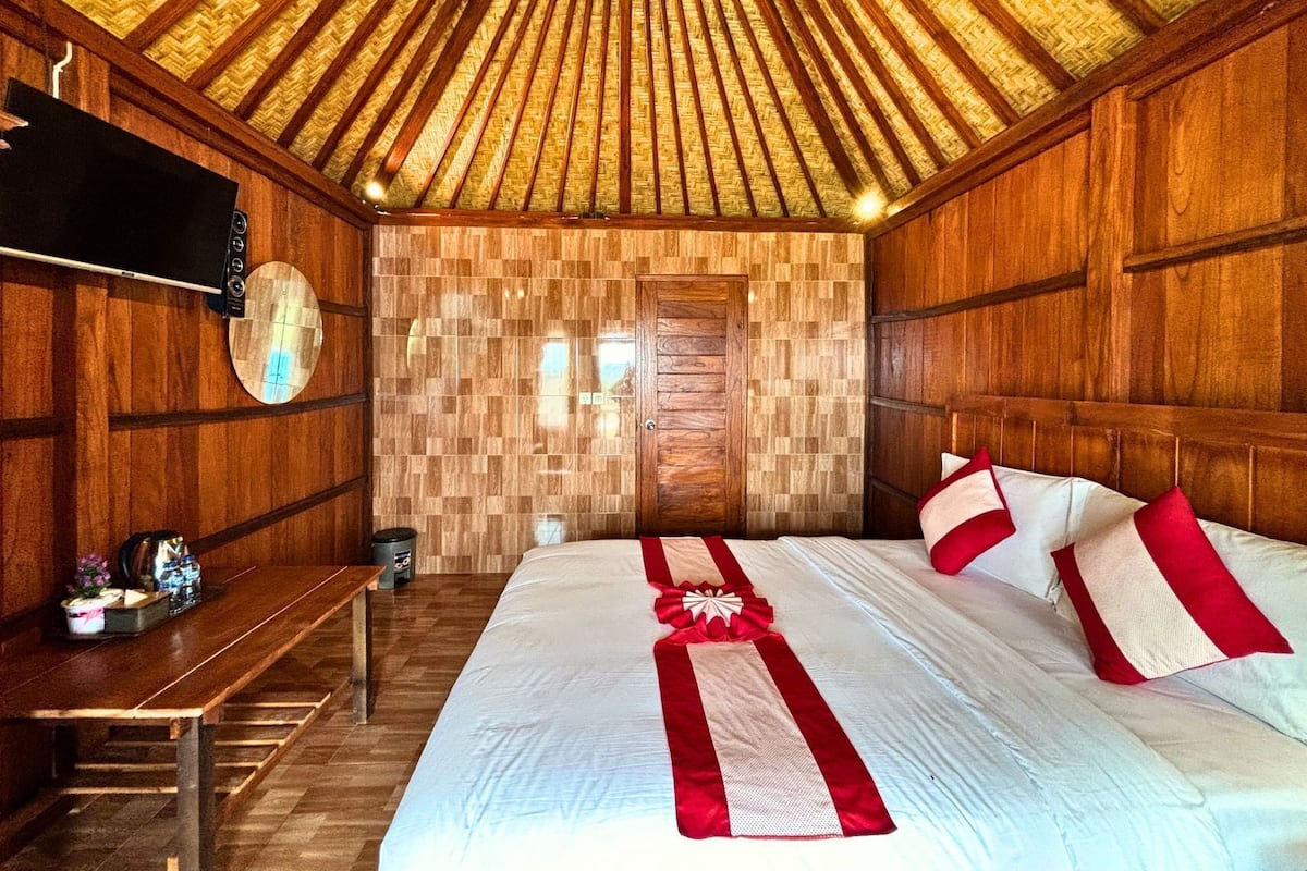 A wooden-paneled room with a bed, a bench, and a television on the wall.