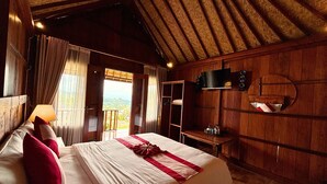 A wooden room with a bed, a TV, a mirror, and a view of the outdoors. - Munduk Luwih Ecolodge Bedugul by AGATA (Baturiti)