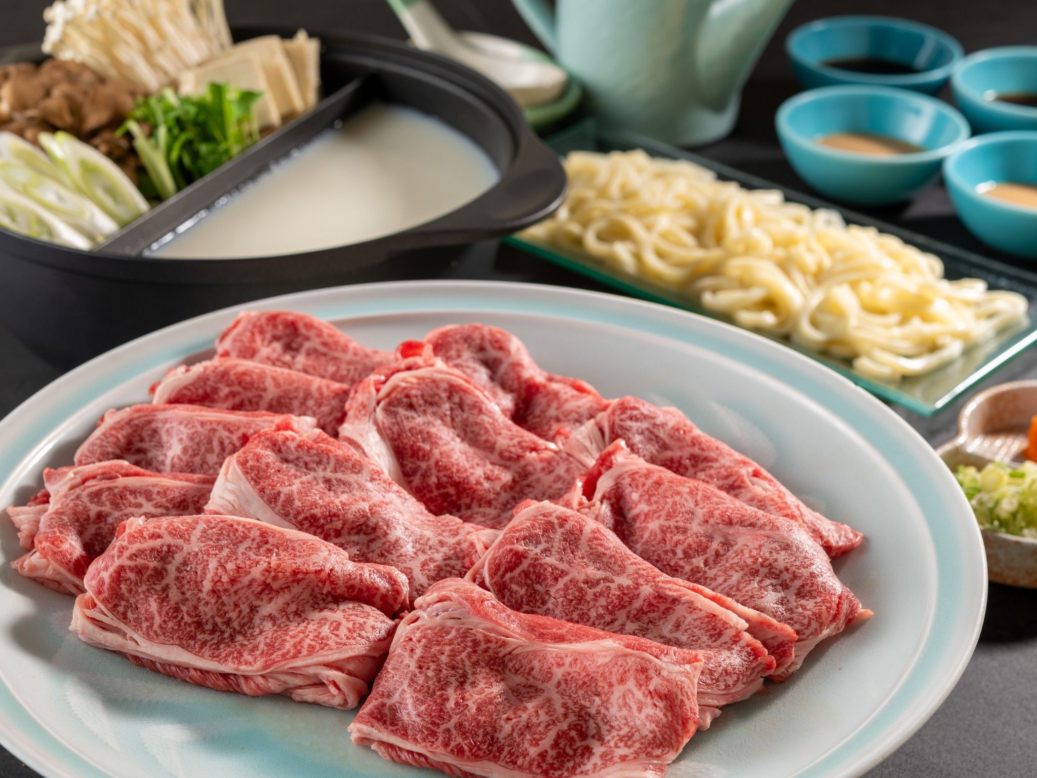 A plate of raw meat, a bowl of noodles, and a hot pot setup.