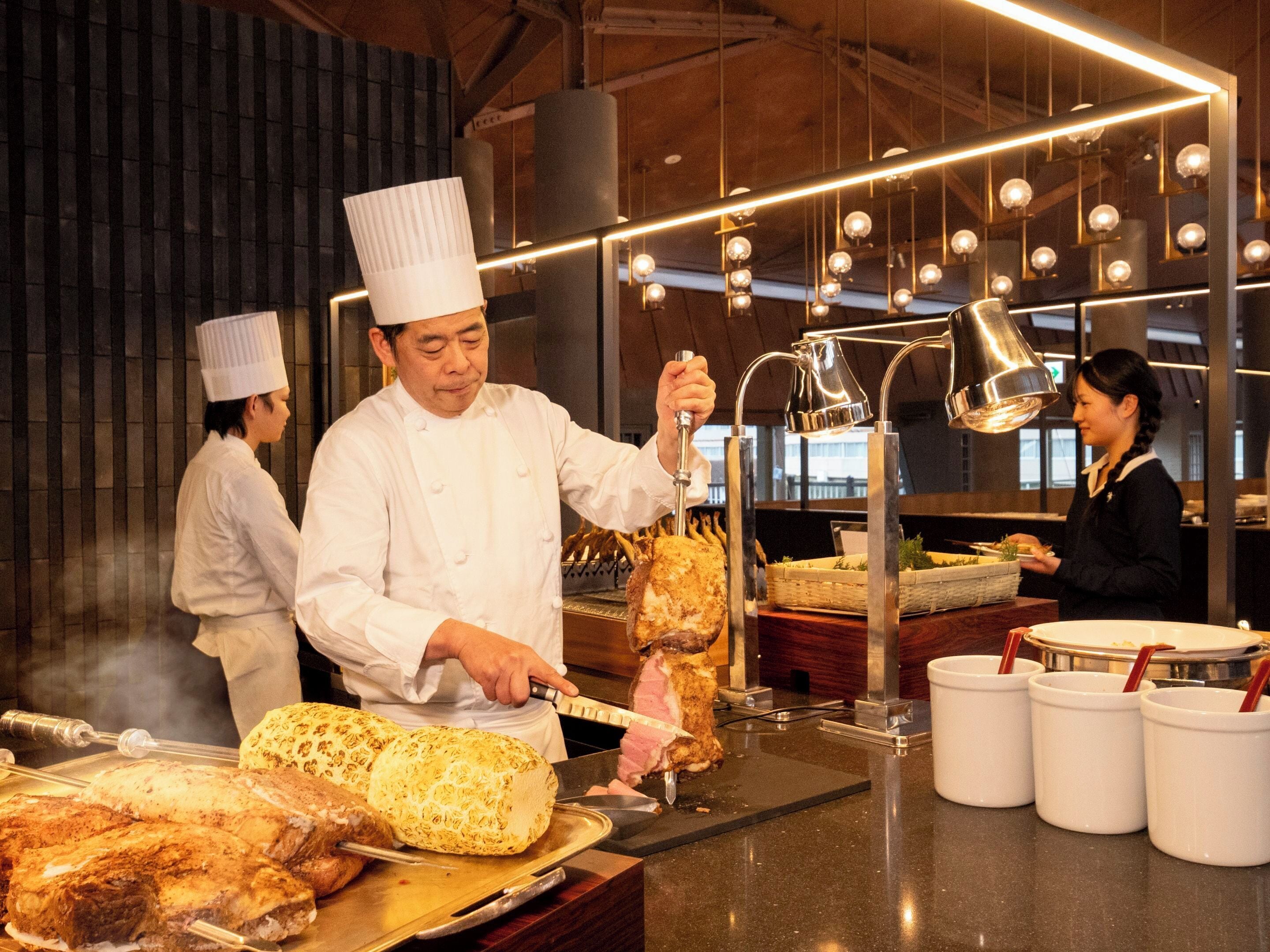 Un chef preparando comida en una cocina con una parrilla grande y luces colgantes.