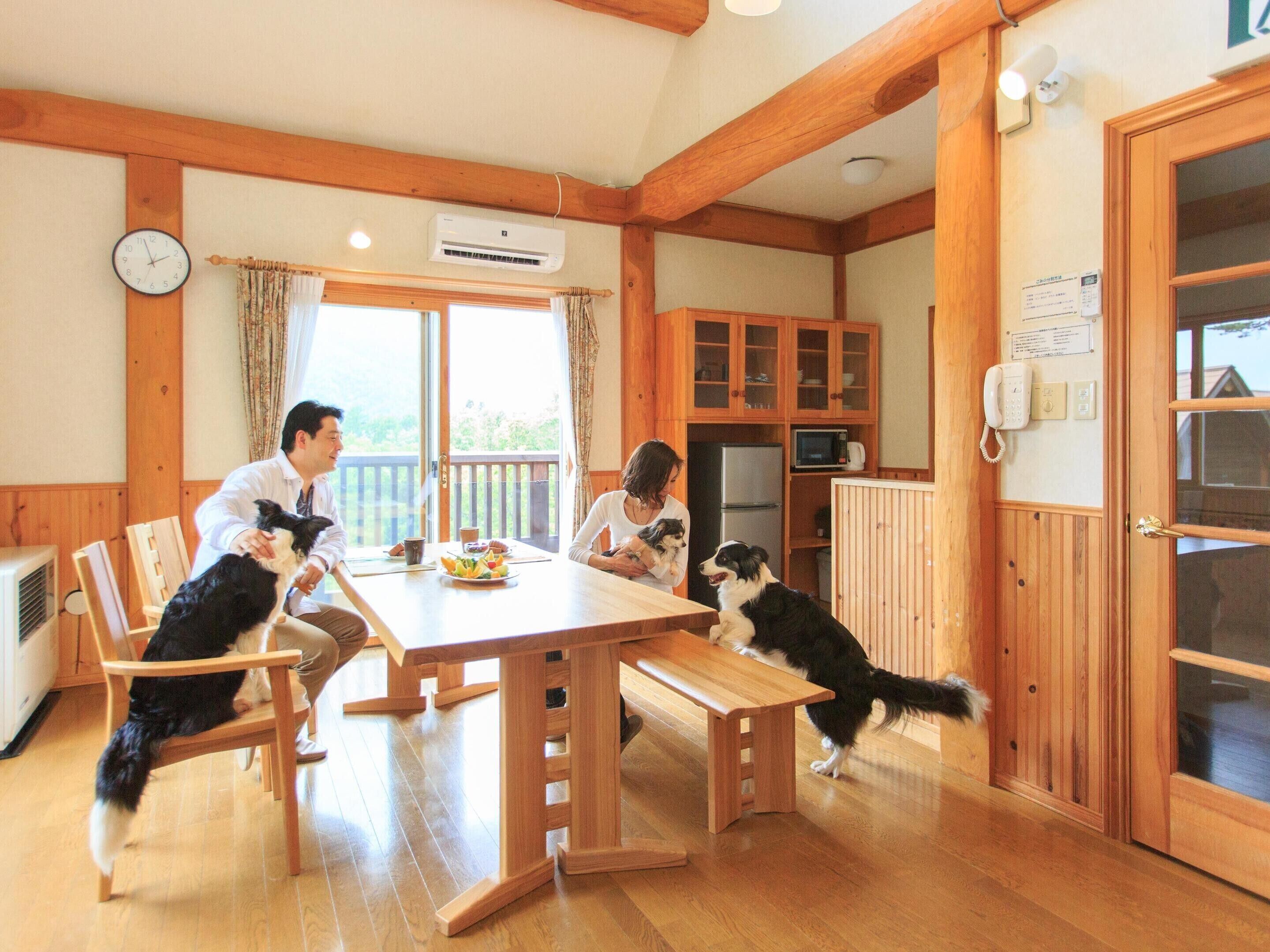 A wooden interior with a dining table, chairs, a clock, an air conditioning unit, a kitchen area with cabinets, a refrigerator, and a telephone.