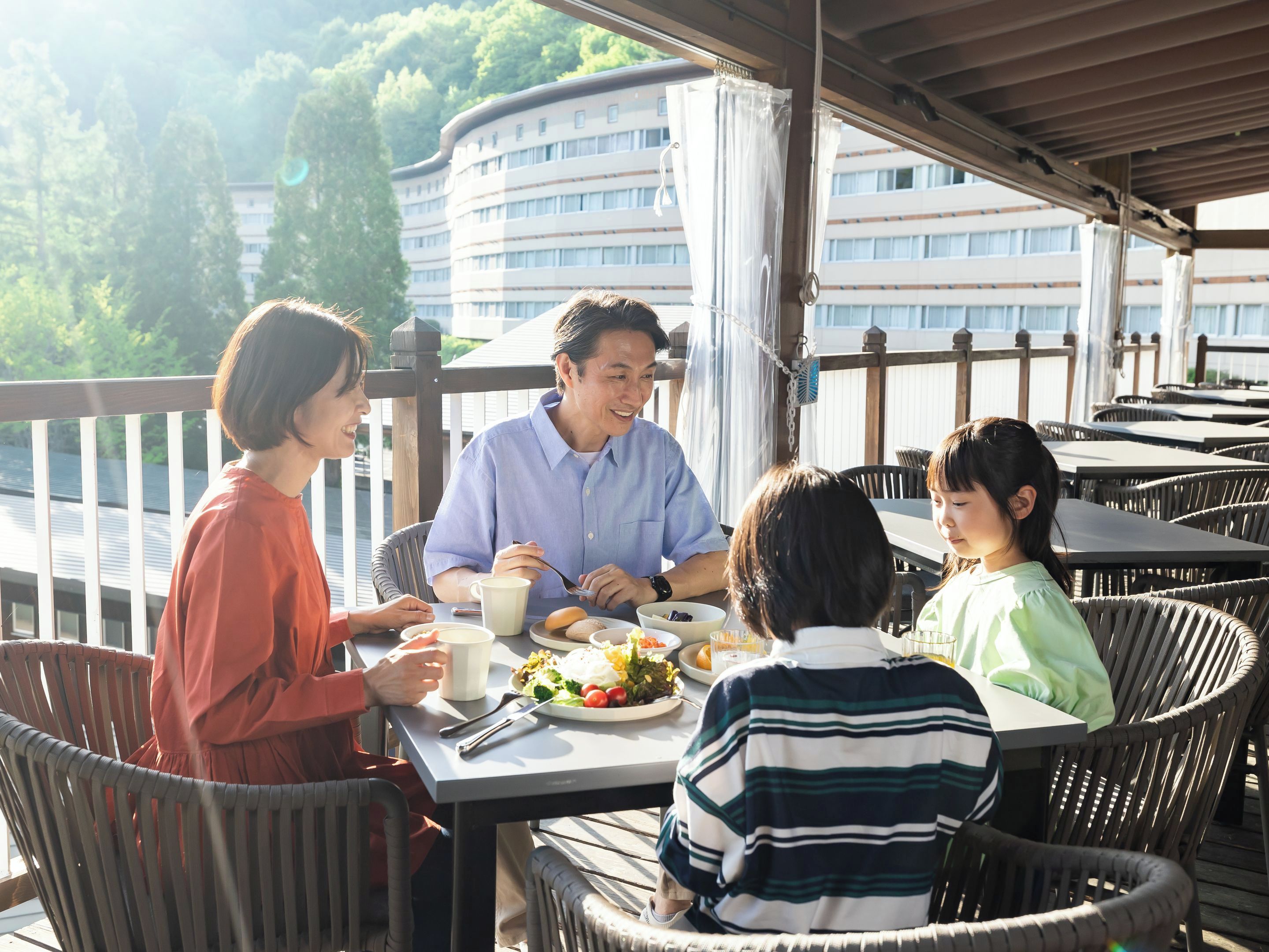 A group of people dining at an outdoor table with a view of a building and trees in the background.