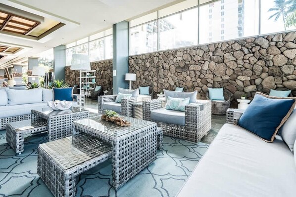 A modern lounge area with wicker furniture, a stone wall, and large windows.