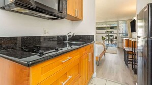 A modern kitchen with wooden cabinets, a black countertop, a stainless steel microwave, and a built-in oven. - @Marbella Lane - Stylish Island Stay w/ City Views (Honolulu)
