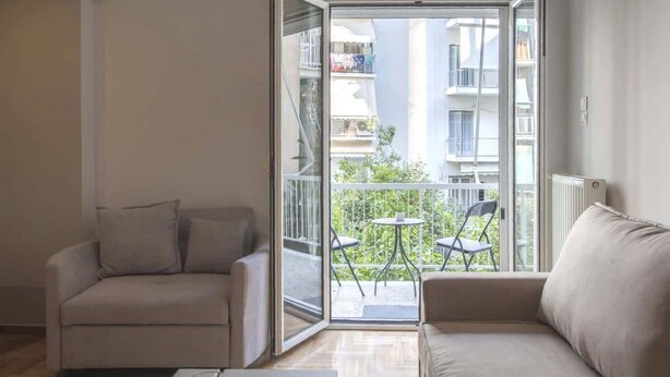 A living room with a sofa, a coffee table, and a sliding glass door leading to a balcony with a table and chairs. - "Urban Comfort Stay" (Athina)