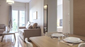 A modern living room with a wooden dining table set for two, a sofa, and a balcony view. - "Urban Comfort Stay" (Athina)
