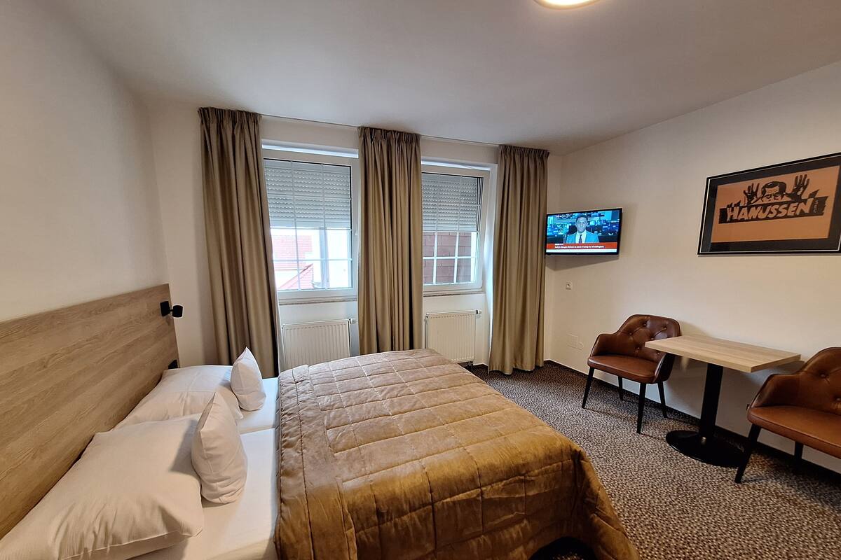 A hotel room with a bed, a desk, a chair, a television, and a window with curtains.