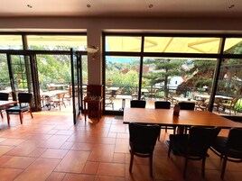 Un'area pranzo interna con ampie finestre, tavoli e sedie in legno.