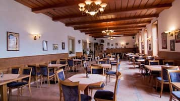Un restaurante espacioso con mesas y sillas de madera, techos altos con vigas a la vista e iluminación instalada en la pared.