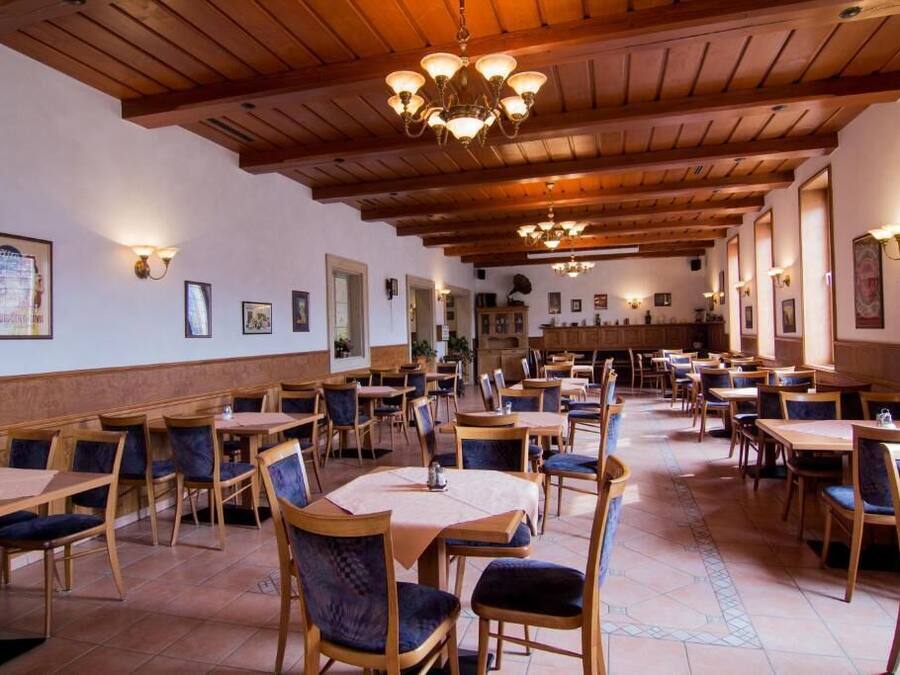 Un restaurante espacioso con mesas y sillas de madera, techos altos con vigas a la vista e iluminación instalada en la pared.