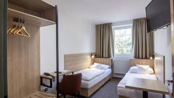 A hotel room with two beds, a desk, a chair, a TV, and a window with curtains.