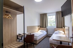Quarto de hotel com duas camas, uma escrivaninha, uma cadeira, televisão e janela com cortinas.