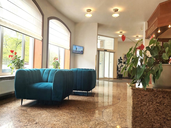 A lobby with a teal sofa, a television mounted on the wall, and a reception desk.