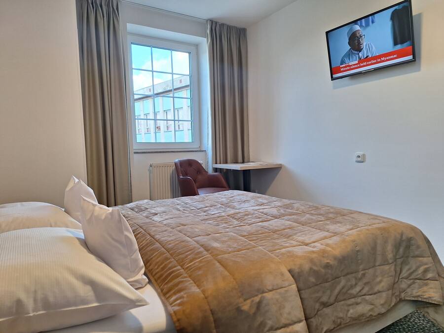 A hotel room with a bed, a chair, a desk, a television, and a window with curtains.
