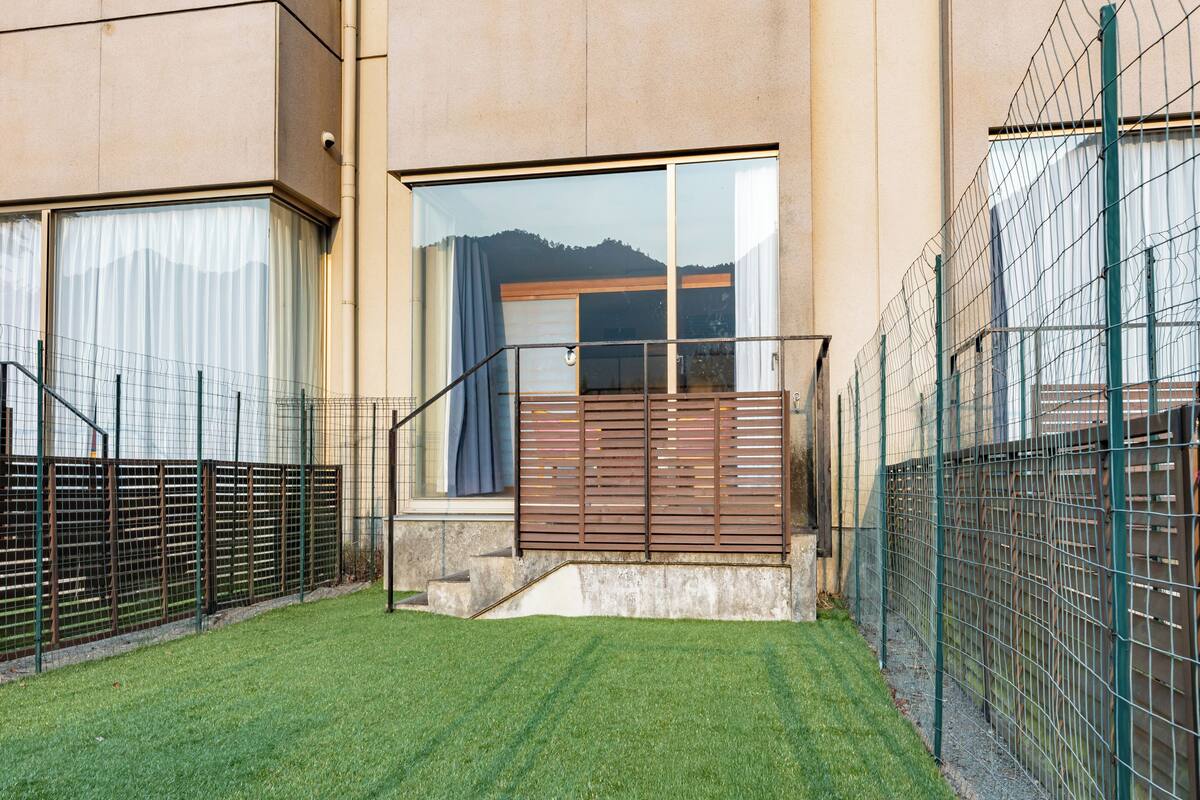 A modern building with a well-maintained lawn, a wooden staircase leading to a balcony, and a metal fence.