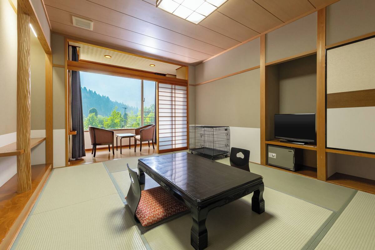 A traditional Japanese room with tatami flooring, a low table, a TV, and a view of the outdoors.