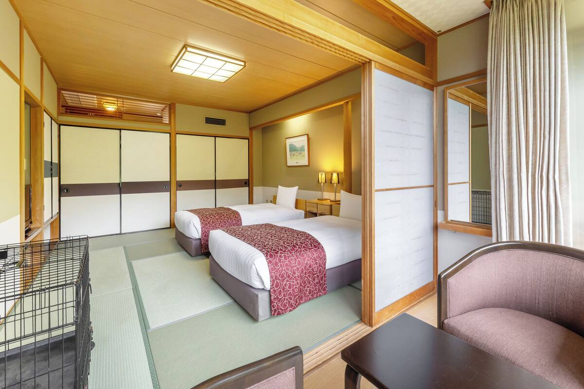 A traditional Japanese-style hotel room with two beds, a tatami mat floor, a wooden ceiling, and a sliding door.