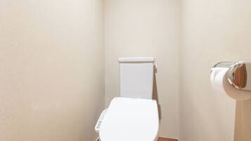 A small, compact bathroom with a white toilet, a wooden floor, and a plain wall.