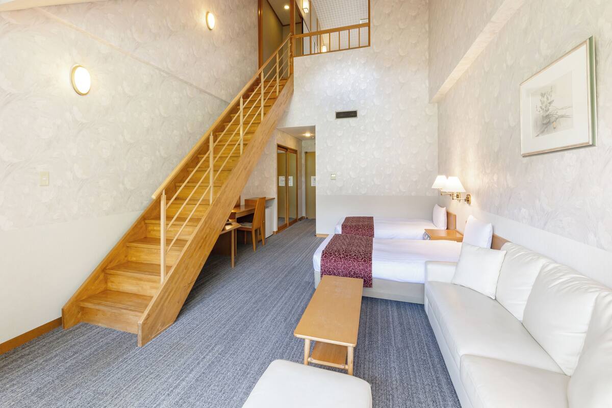 A hotel room with a wooden staircase, a sofa, a small table, and a bed.