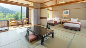 Habitación de estilo japonés tradicional con suelo de tatami, una mesa baja, dos camas y vistas a un área boscosa.