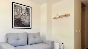 En moderne stue med en grå sofa, et billede af en bysilhuet i ramme, et lille bord med en vandflaske og en træhylde med pynt.