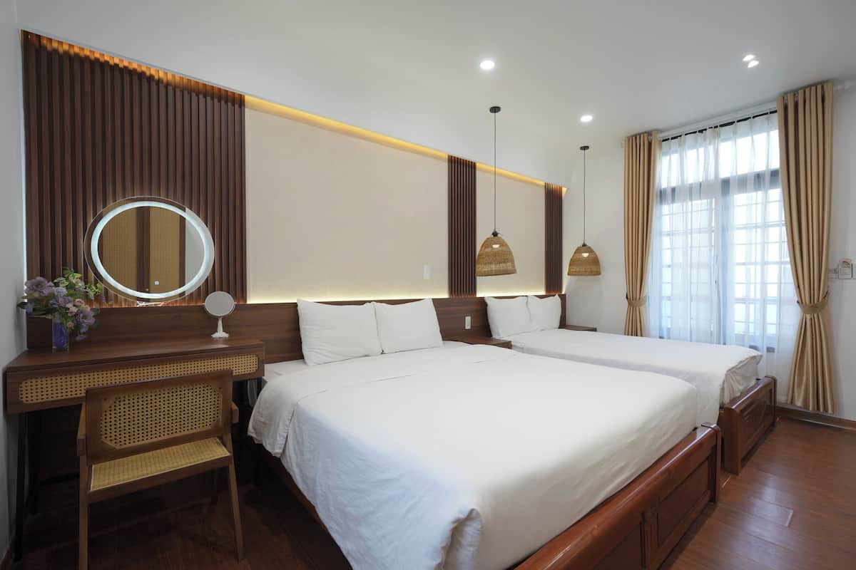 A hotel room with two beds, a bedside table with a mirror, a small chair, and a decorative vase.