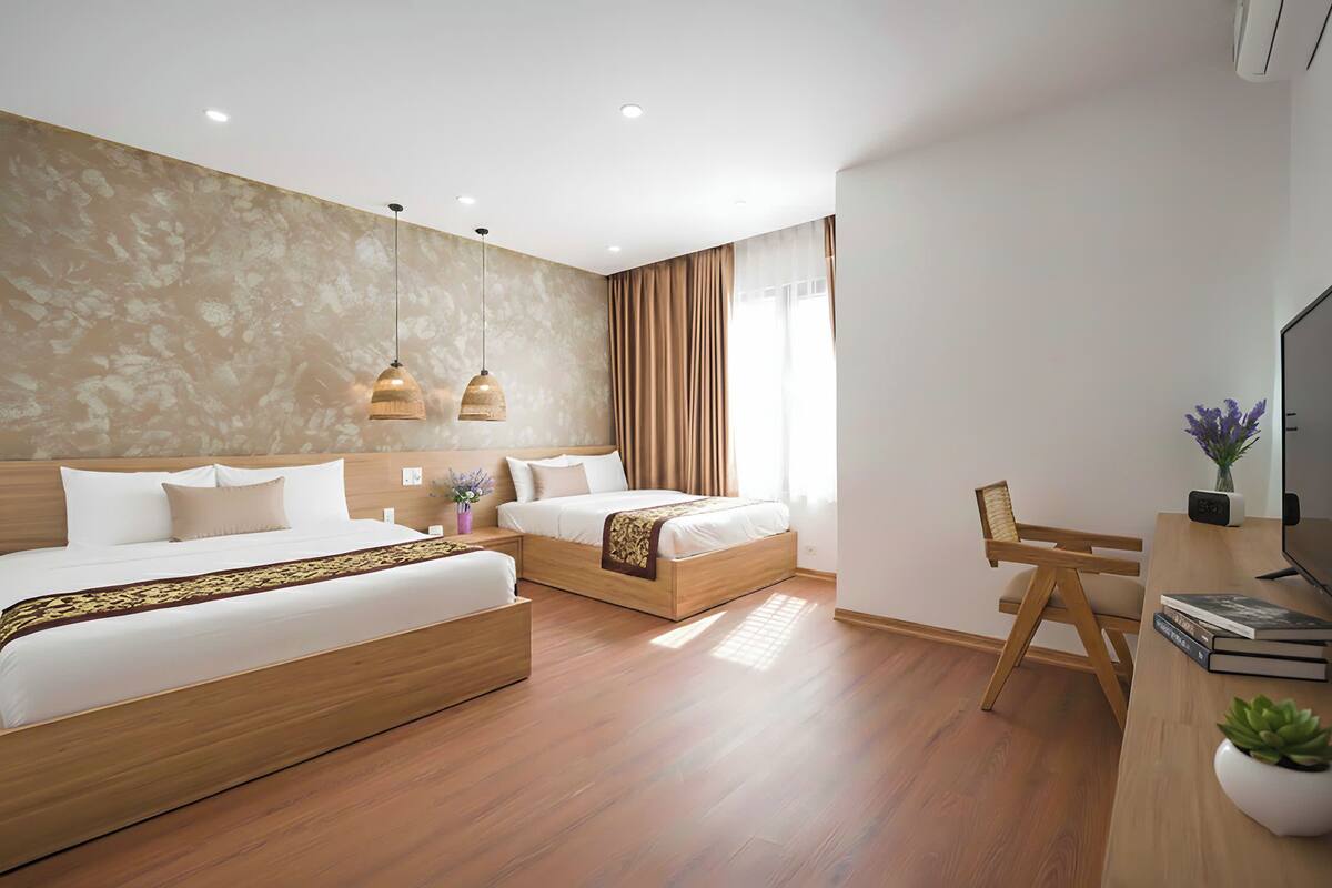 A modern hotel room with two beds, a desk with a chair, a TV, and a large window with curtains.