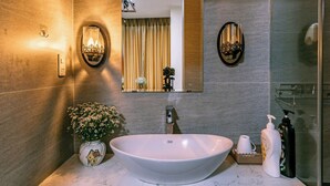 A bathroom with a large oval sink, a mirror, a vase with flowers, and toiletries on the counter. - Nana House Homestay (Hue)