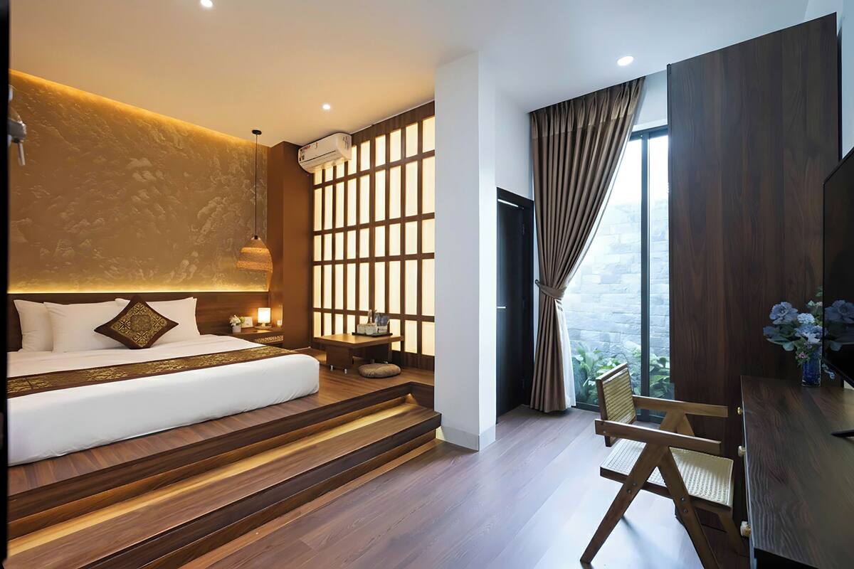 A modern bedroom with a bed, a wooden desk, a chair, and a view of the outdoors.