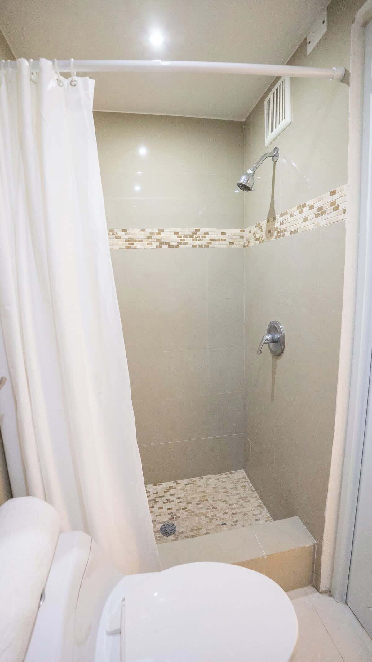 A shower with a glass door, a showerhead, and a tiled floor.