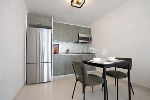 Una cucina moderna con frigorifero in acciaio inox, forno a microonde e zona pranzo con due sedie e un tavolo imbandito per due persone.
